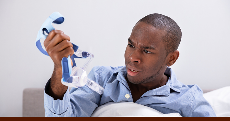 Irritated looking man holding a CPAP mask to illustrate that this article talks about treating sleep apnea with oral appliances