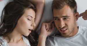 A man looking at his female partner snoring with obstructive sleep apnea in annoyance